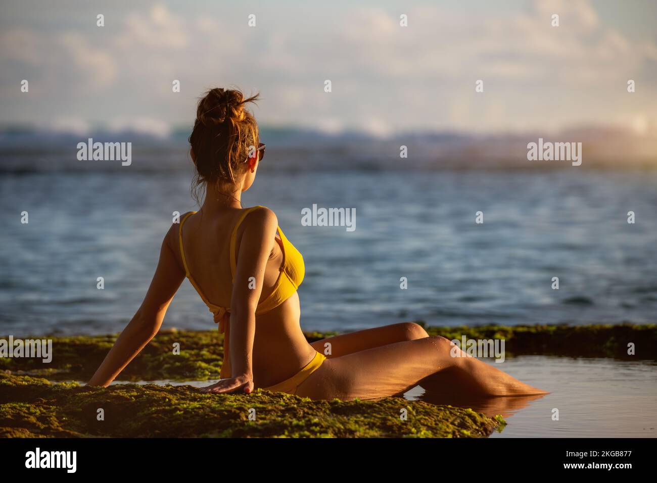 Bella ragazza giovane in costume da bagno siede al tramonto spiaggia oceano e rilassarsi Foto Stock