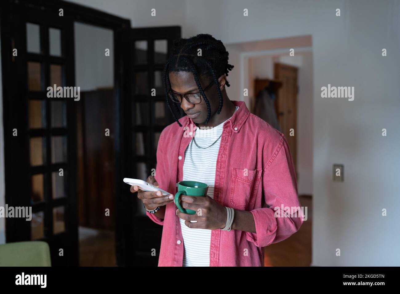 Uomo africano americano concentrato pensivo con telefono si alza in casa e scrive messaggio agli amici Foto Stock