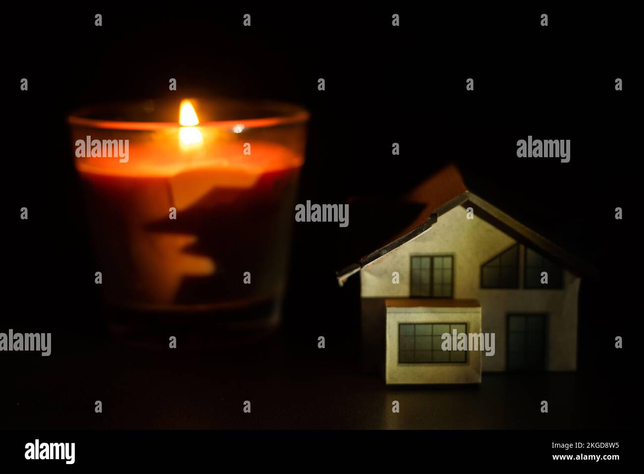 una candela e una casa giocattolo su sfondo scuro Foto Stock