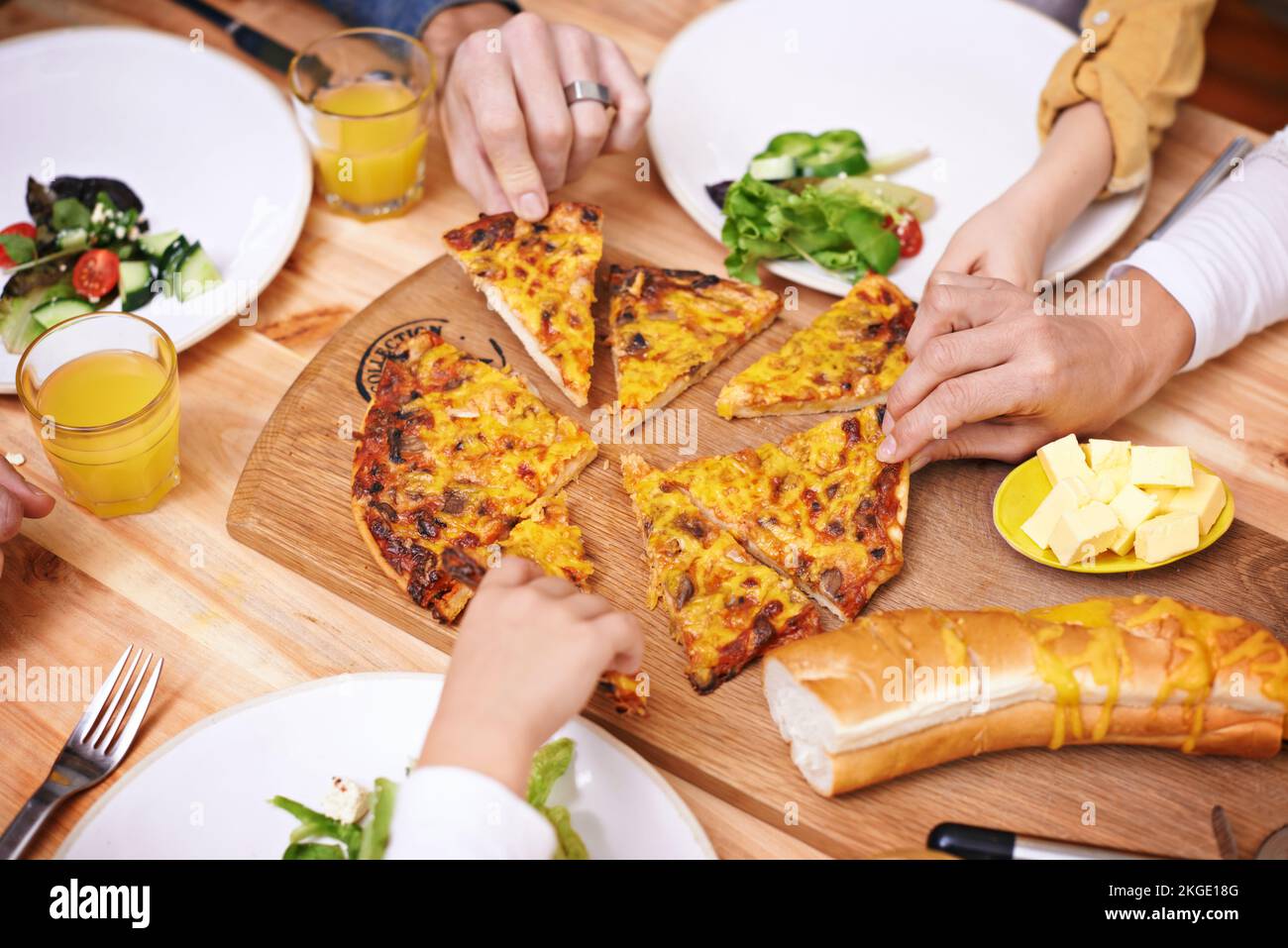 Rimettiti in sede. una famiglia con le mani che si avvicinano per le fette della pizza durante la cena. Foto Stock