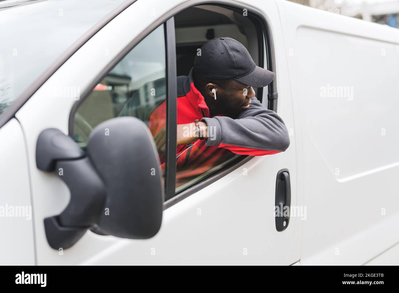 Giovane adulto nero che porta con sé un furgone bianco che appoggia il gomito sulla porta e che si affaccia sulla finestra guardando dietro. Scatto orizzontale. Foto di alta qualità Foto Stock