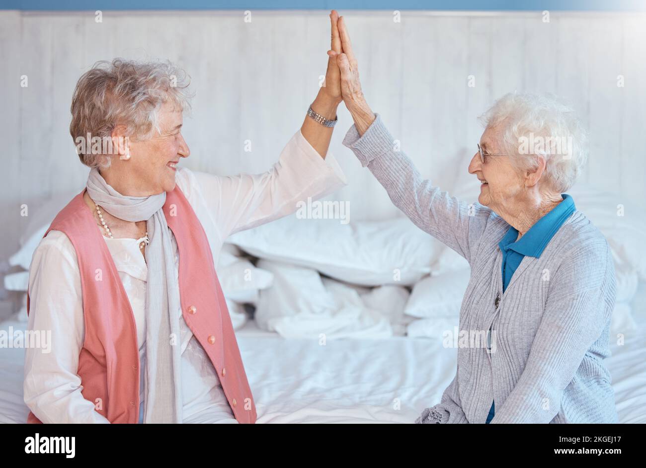 Donna anziana, amici alti cinque e seduti in camera da letto con sorriso, felice o insieme in casa di cura. Donne anziane, migliori amici e felicità con Foto Stock