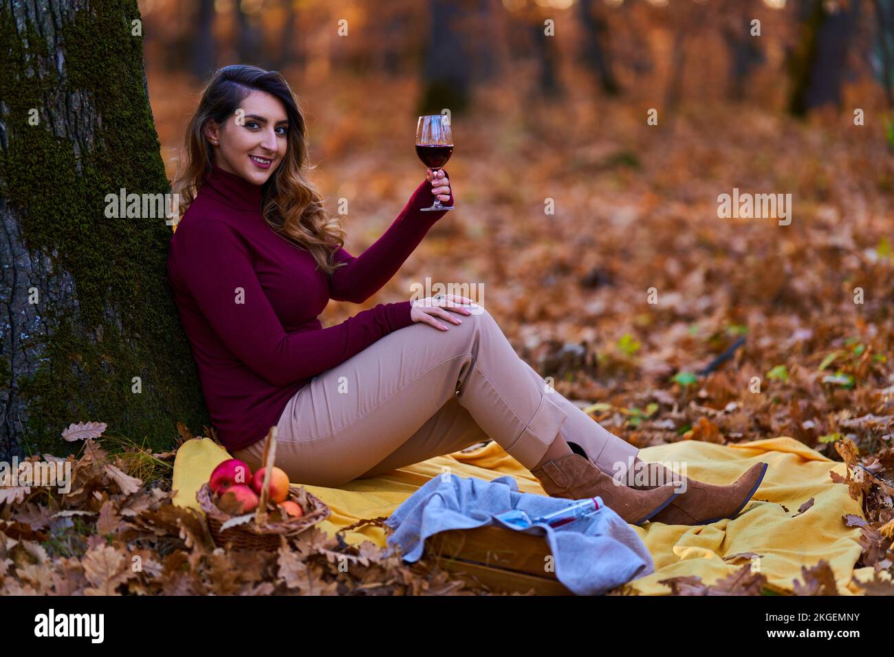 Bella giovane donna indiana di dimensioni più grandi che si gode un bicchiere di vino rosso nella foresta di querce al tramonto Foto Stock
