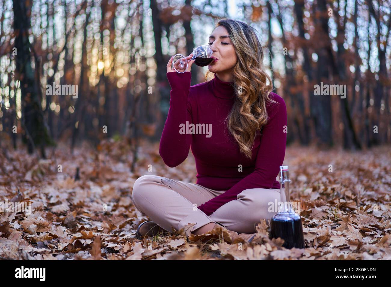 Bella giovane donna indiana di dimensioni più grandi che si gode un bicchiere di vino rosso nella foresta di querce al tramonto Foto Stock