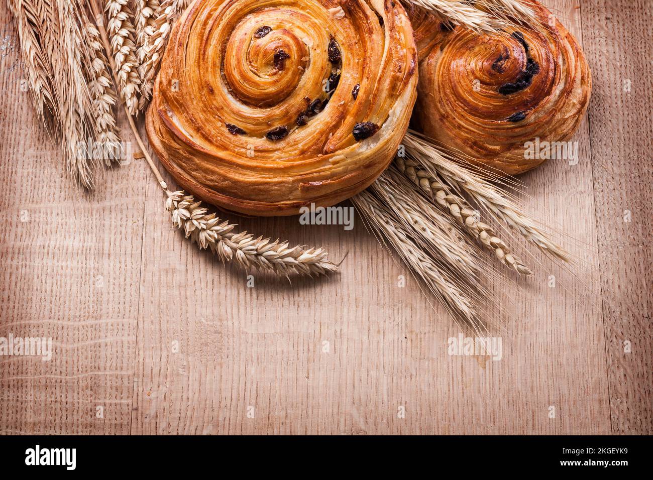 Involtini al forno con uva passa maturi alle orecchie di grano su tavola di legno di legno e bevande Foto Stock