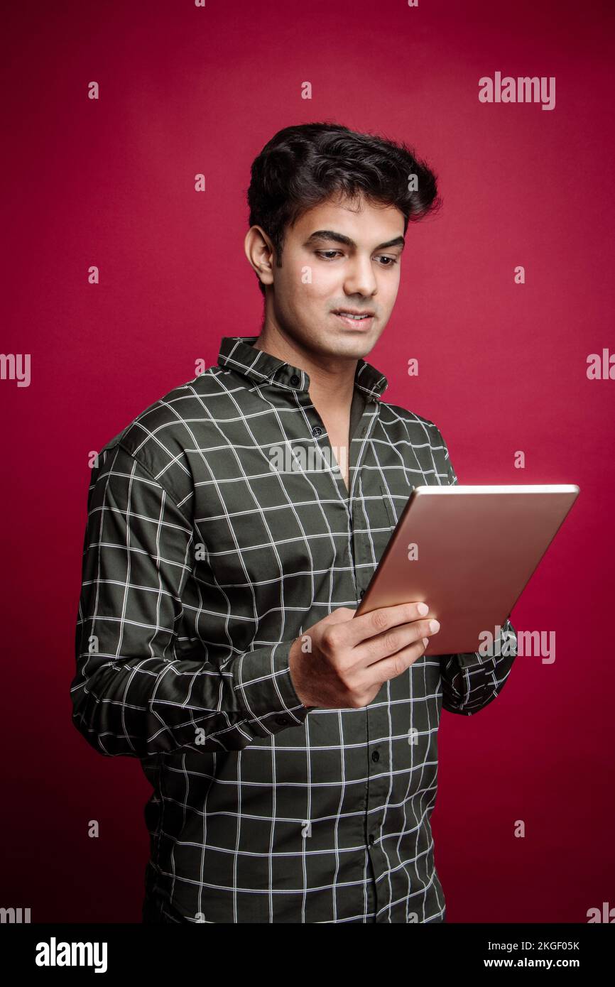 Giovane uomo d'affari indiano sorridente, professionista arabo, freelance, gestore di gioielli, e uomo d'affari che tiene un tablet e in piedi in uno studio di background Foto Stock