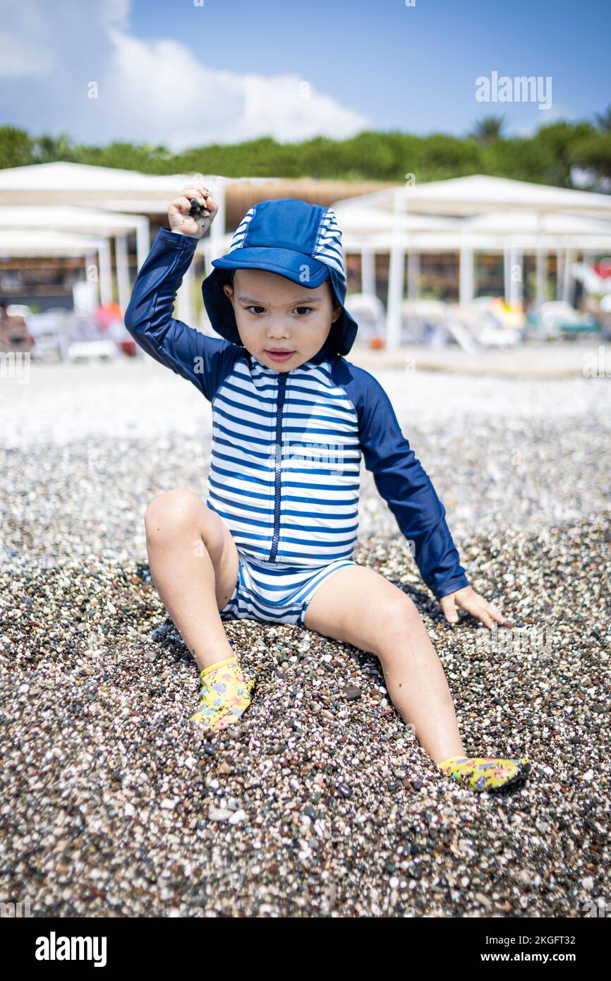 Il bambino in costume gioca con i ciottoli sulla riva del mare in hotel Foto Stock