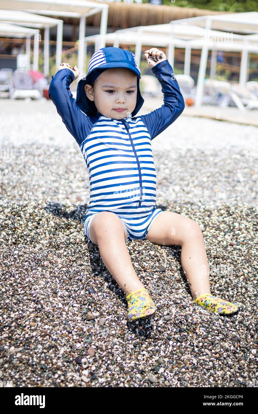 Il bambino in costume gioca con i ciottoli sulla riva del mare in hotel Foto Stock