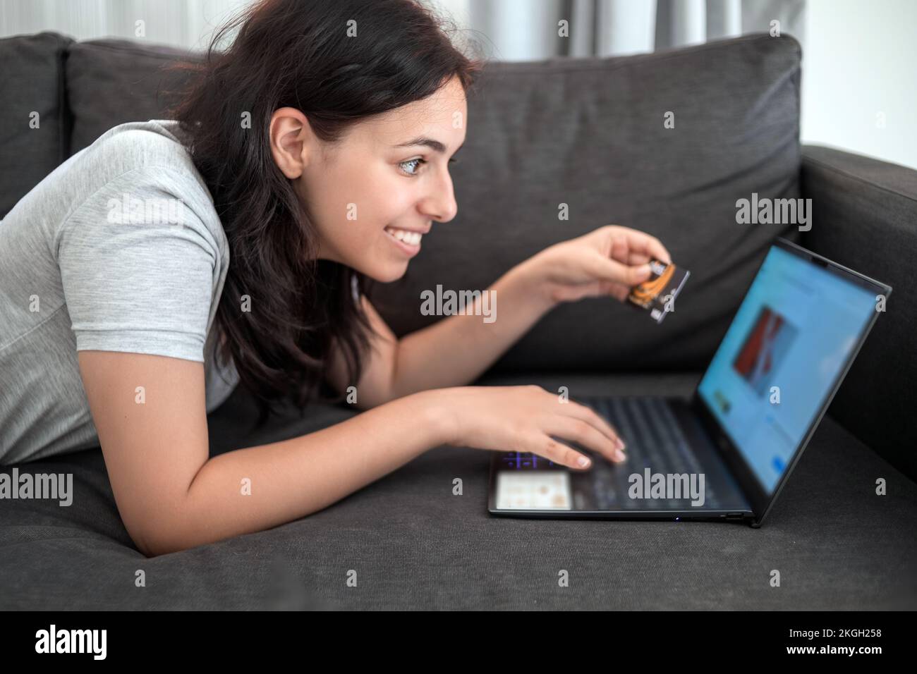 Ragazza giovane che acquista online con carta di credito sul laptop mentre sdraiata sul divano Foto Stock