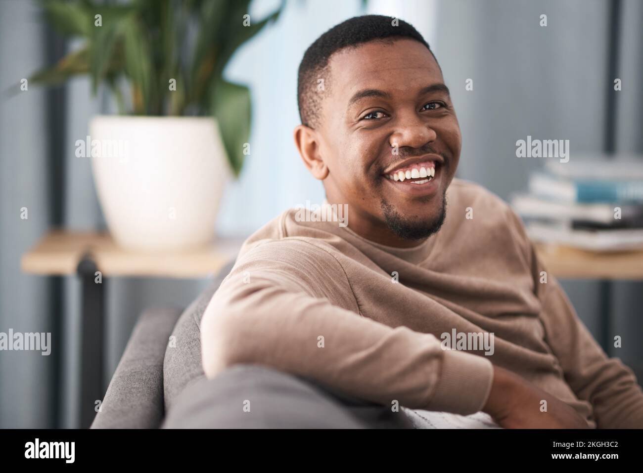 Volto, sorriso e ritratto di un uomo nero rilassarsi in un soggiorno in una casa in vacanza, pausa o fine settimana. Felicità, calma e giovane maschio seduto da solo Foto Stock