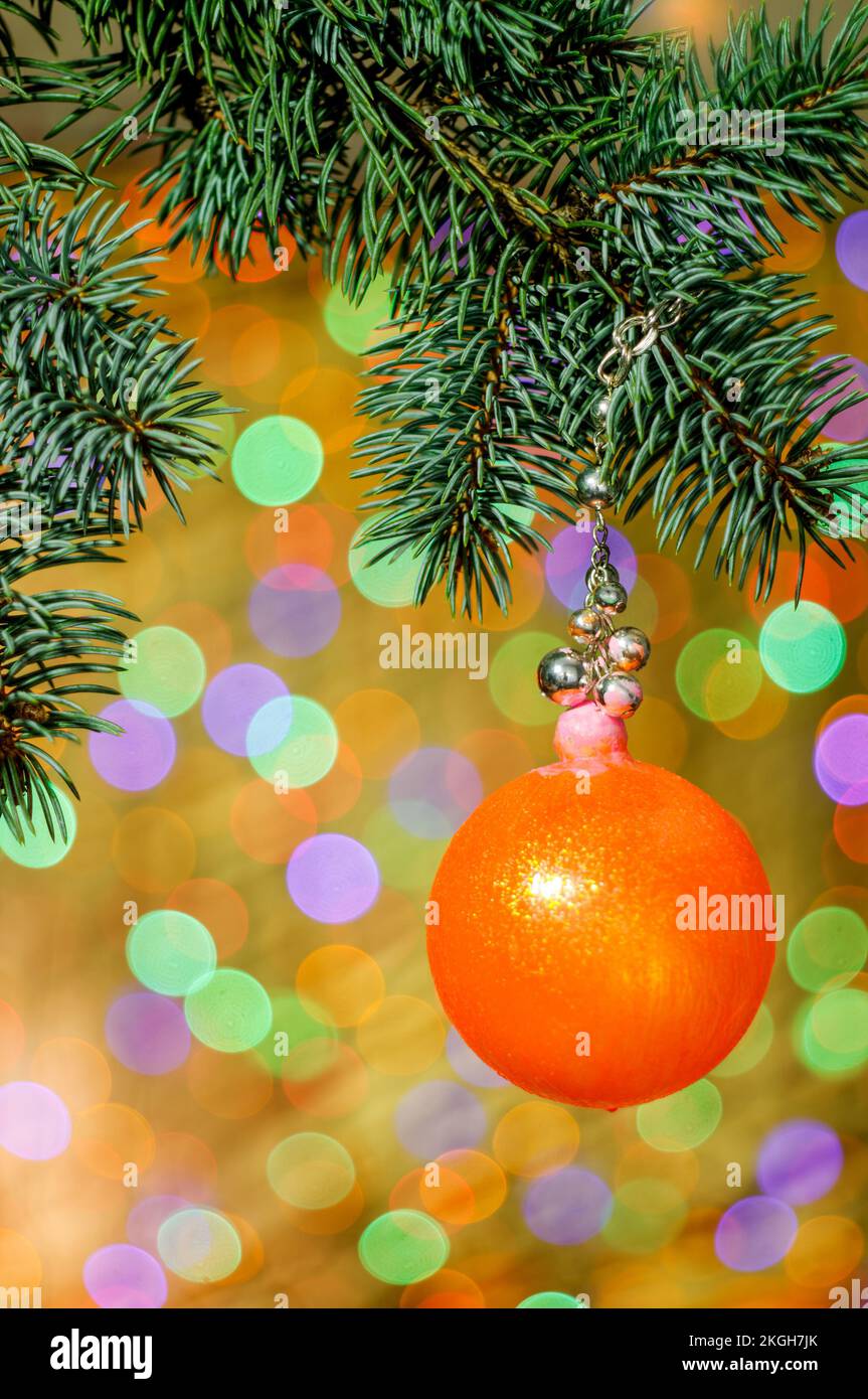 cupola decorativa arancione di natale appesa a una catena decorativa da un ramoscello con illuminazione colorata con bokeh sullo sfondo, spazio per il testo, colo Foto Stock