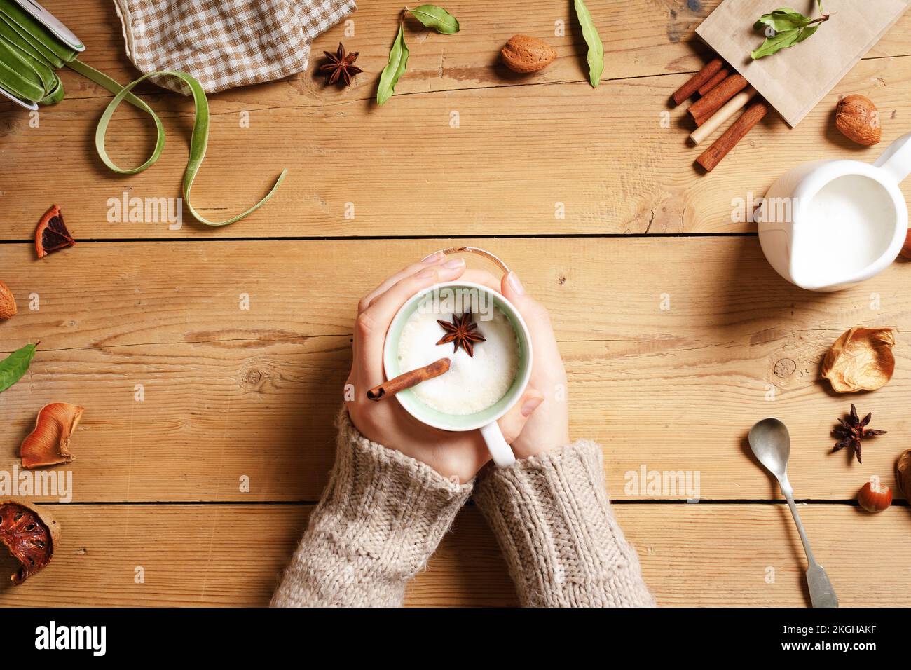 Mano femminile che tiene una tazza con tè indiano Masala chai. Tradizionale bevanda calda indiana con latte e spezie su sfondo di legno con tema natalizio Foto Stock