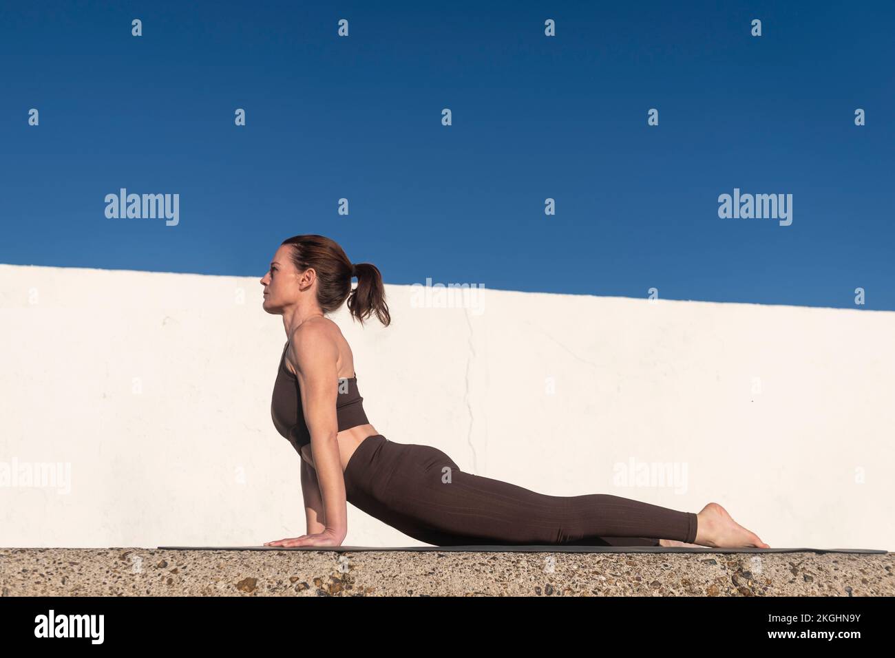 Una donna pratica yoga fuori su un tappeto facendo una posa stretching cobra. Concetto di sport e stile di vita sano. Foto Stock