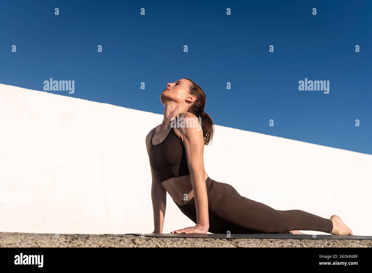 Una donna pratica yoga fuori su un tappeto facendo una posa stretching cobra. Concetto di sport e stile di vita sano. Foto Stock