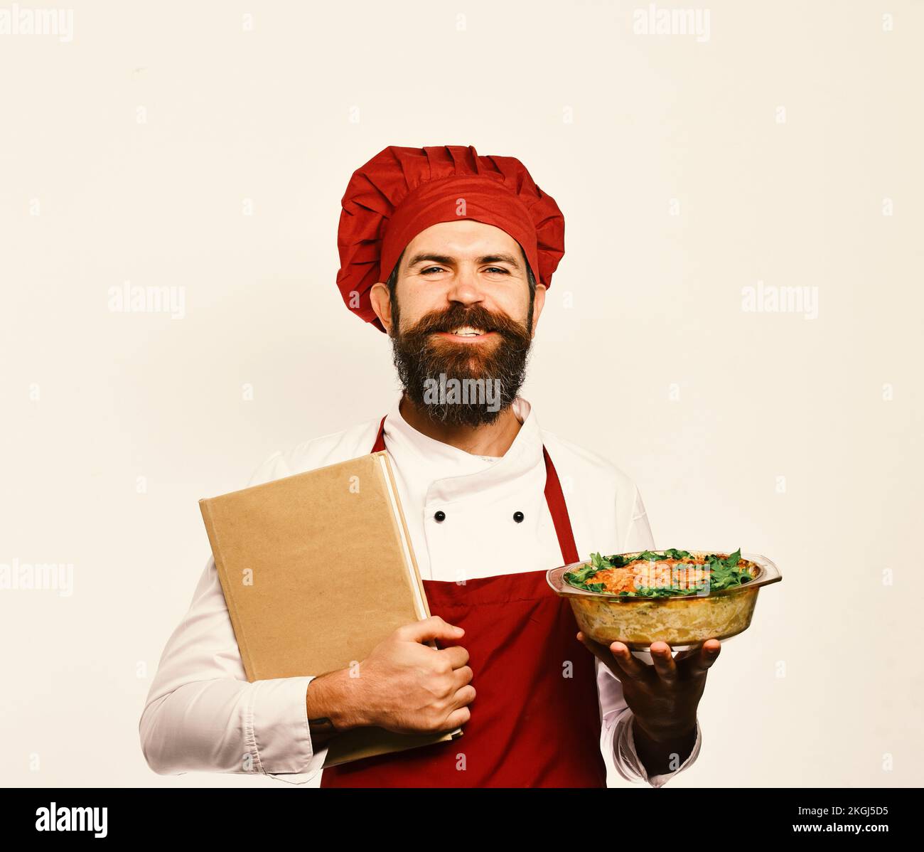 Cucinare con il sorriso orgoglioso in uniforme borgogna tiene piatto al forno Foto Stock