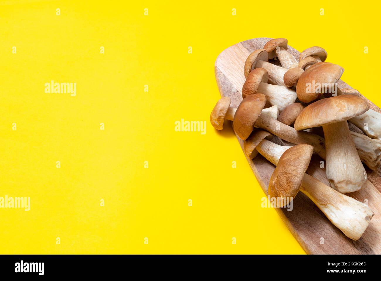 Tappo marrone Boletus Edulis su un tagliere su sfondo giallo. Funghi commestibili su una tavola di legno in cucina. Nessuno Foto Stock