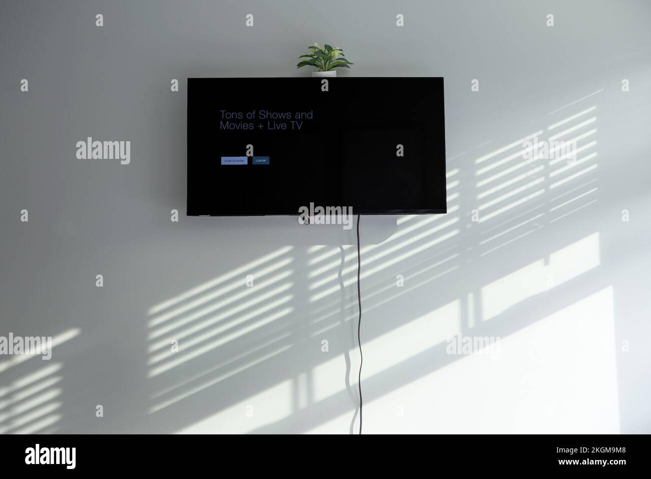 Televisione a grande schermo su una parete della camera da letto con cavo che appende giù con ombre dalle persiane della finestra Foto Stock