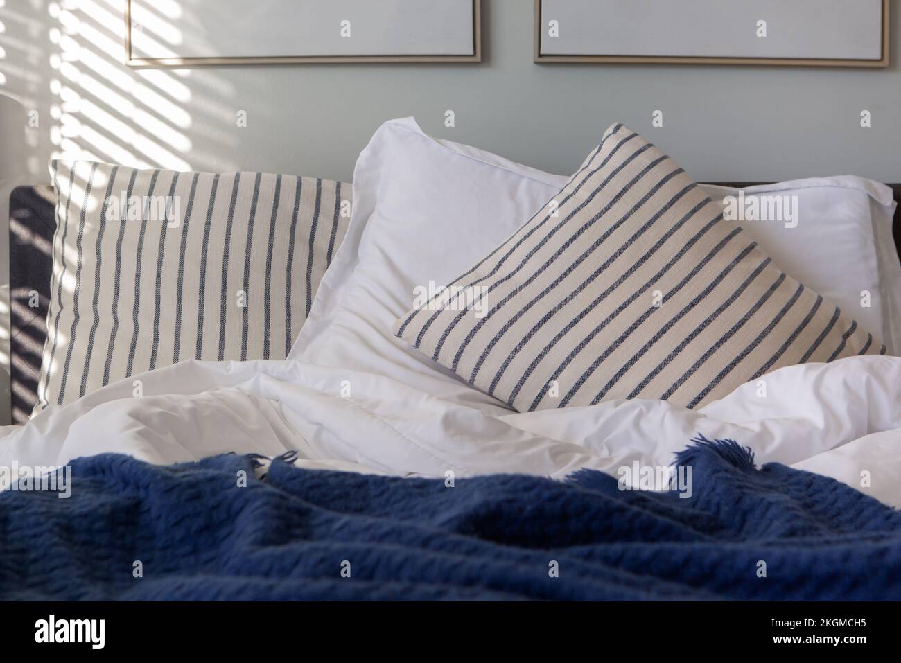 Cuscini a righe e copriletto blu e bianco su un letto alla luce del mattino presto Foto Stock