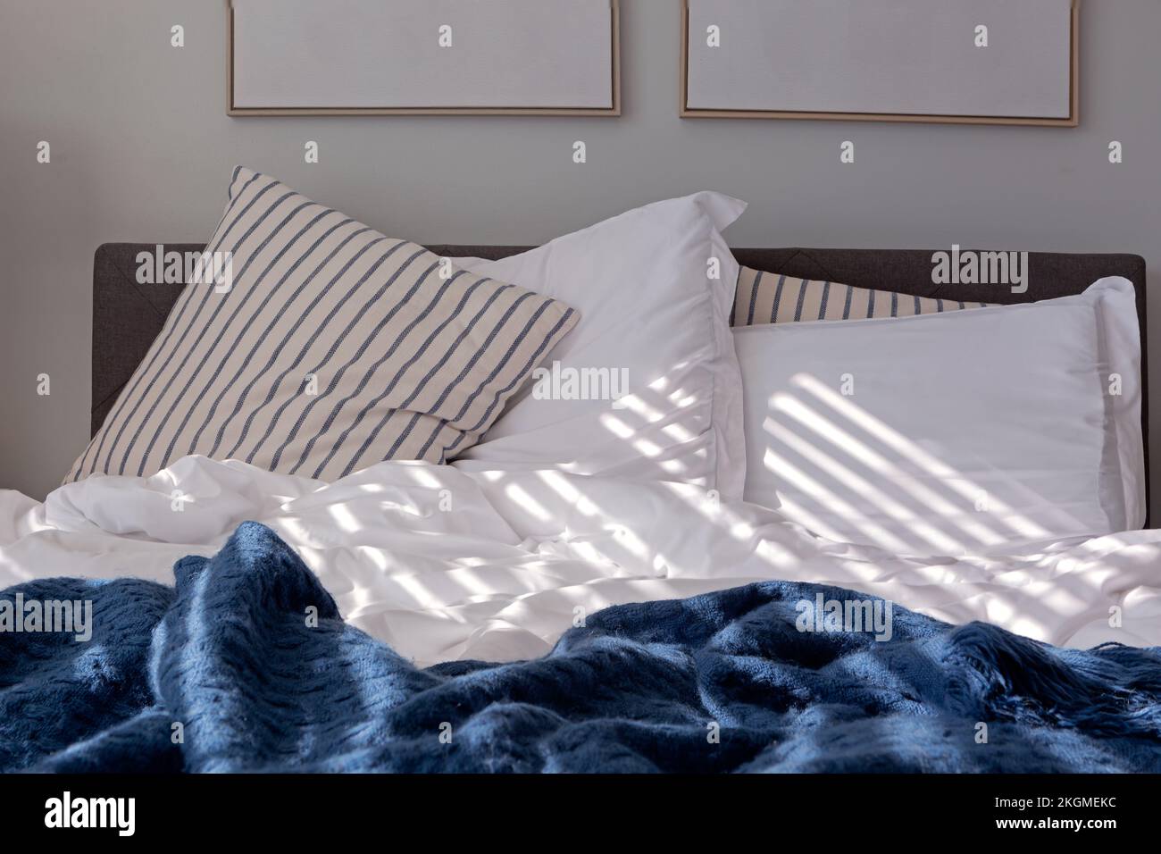 Cuscini a righe e copriletto blu e bianco su un letto alla luce del mattino presto Foto Stock