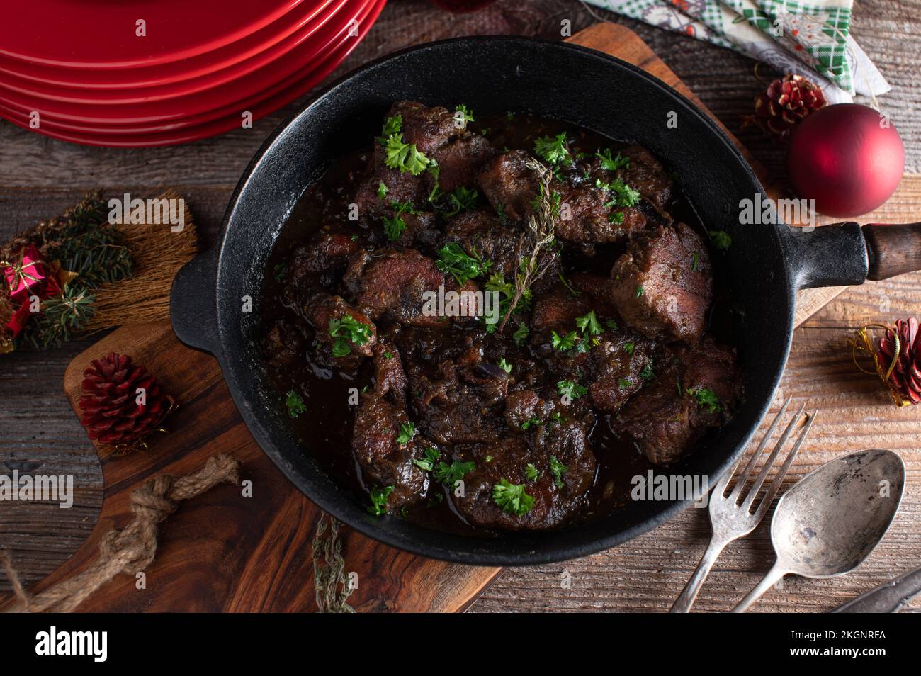 Piatto di carne di Natale con medaglioni di filetto di maiale brasato e salsa di cipolle rosse in una padella rustica su tavola di legno con piatti, tovaglioli e ornamenti. Foto Stock