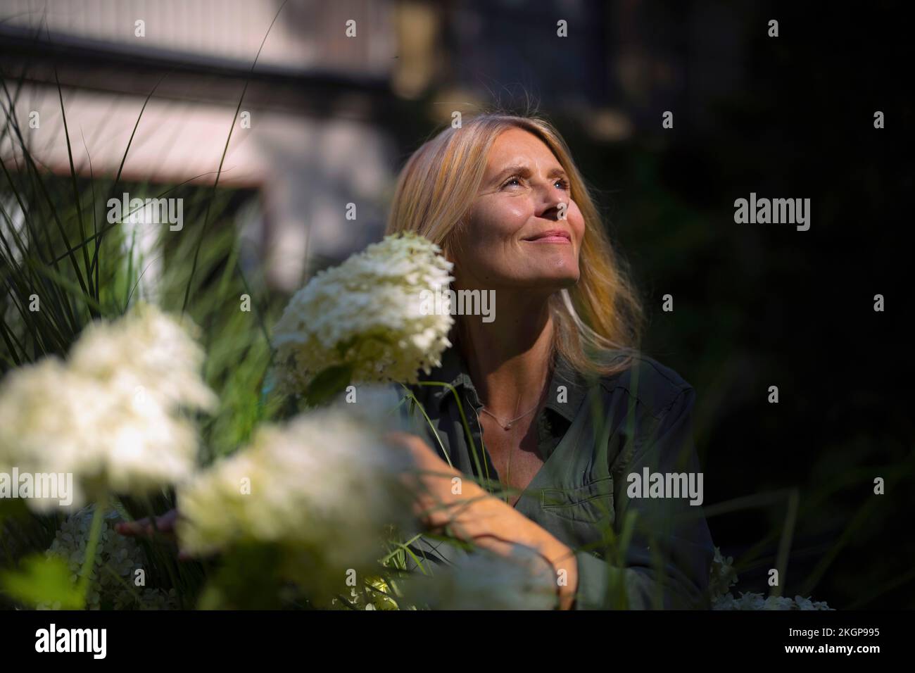 Donna matura sorridente in piedi da piante fiorite in giardino Foto Stock