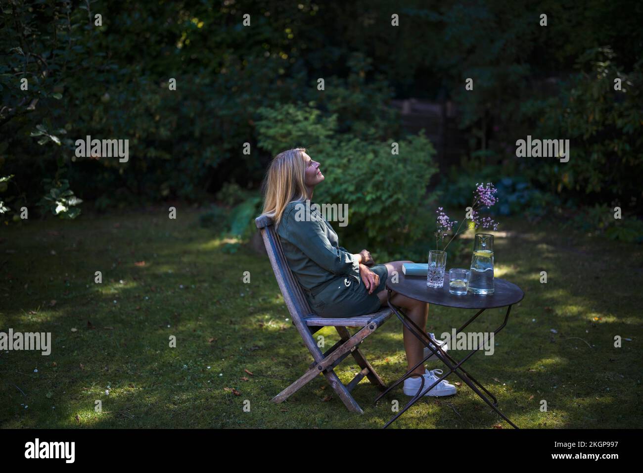 Donna matura pensierosa seduta su sedia in giardino Foto Stock