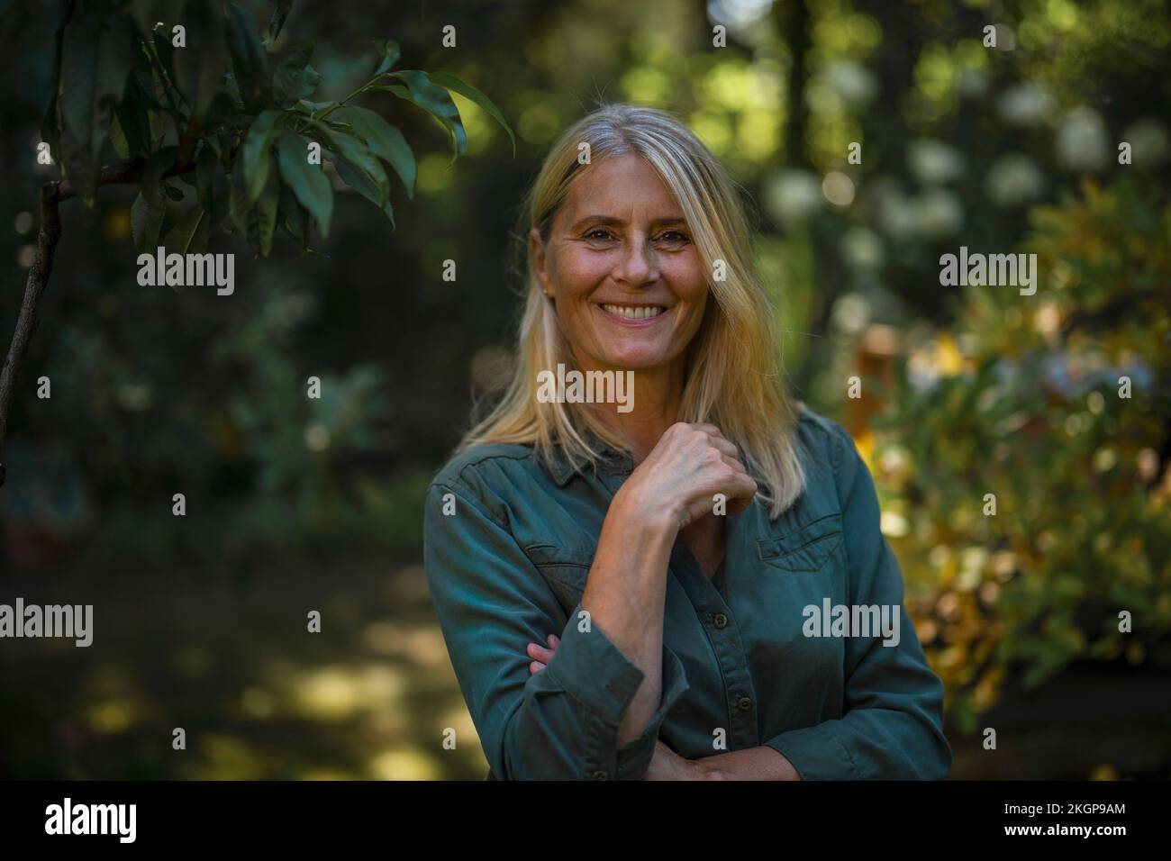 Donna felice con capelli biondi in piedi in giardino Foto Stock