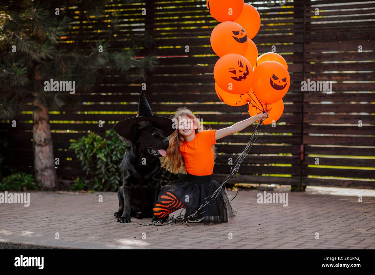Ragazza che tiene palloncini arancioni da cane indossando cappello di strega sul sentiero Foto Stock