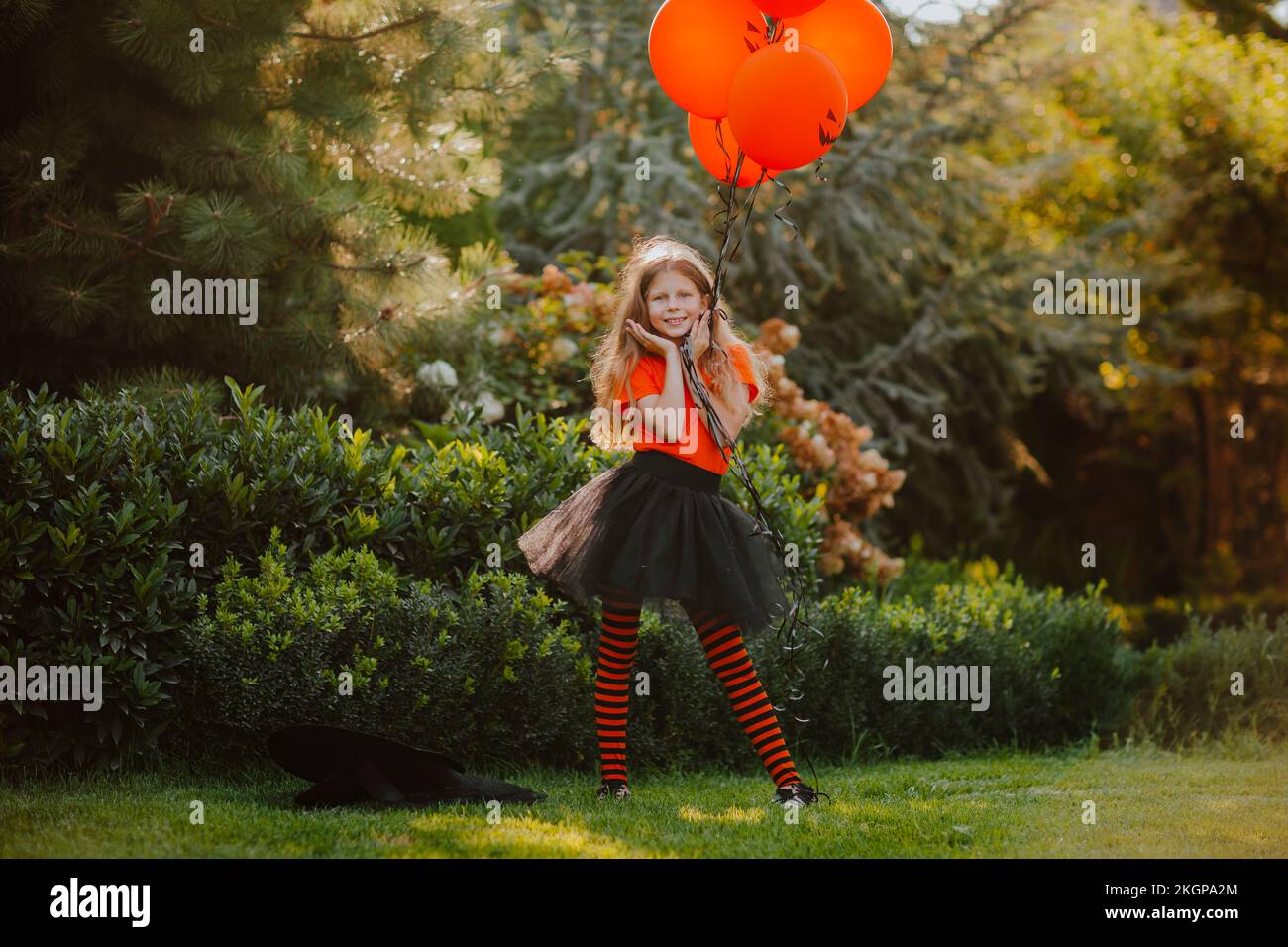 Ragazza sorridente che tiene palloncini arancioni in piedi con la testa in mano al cortile posteriore Foto Stock