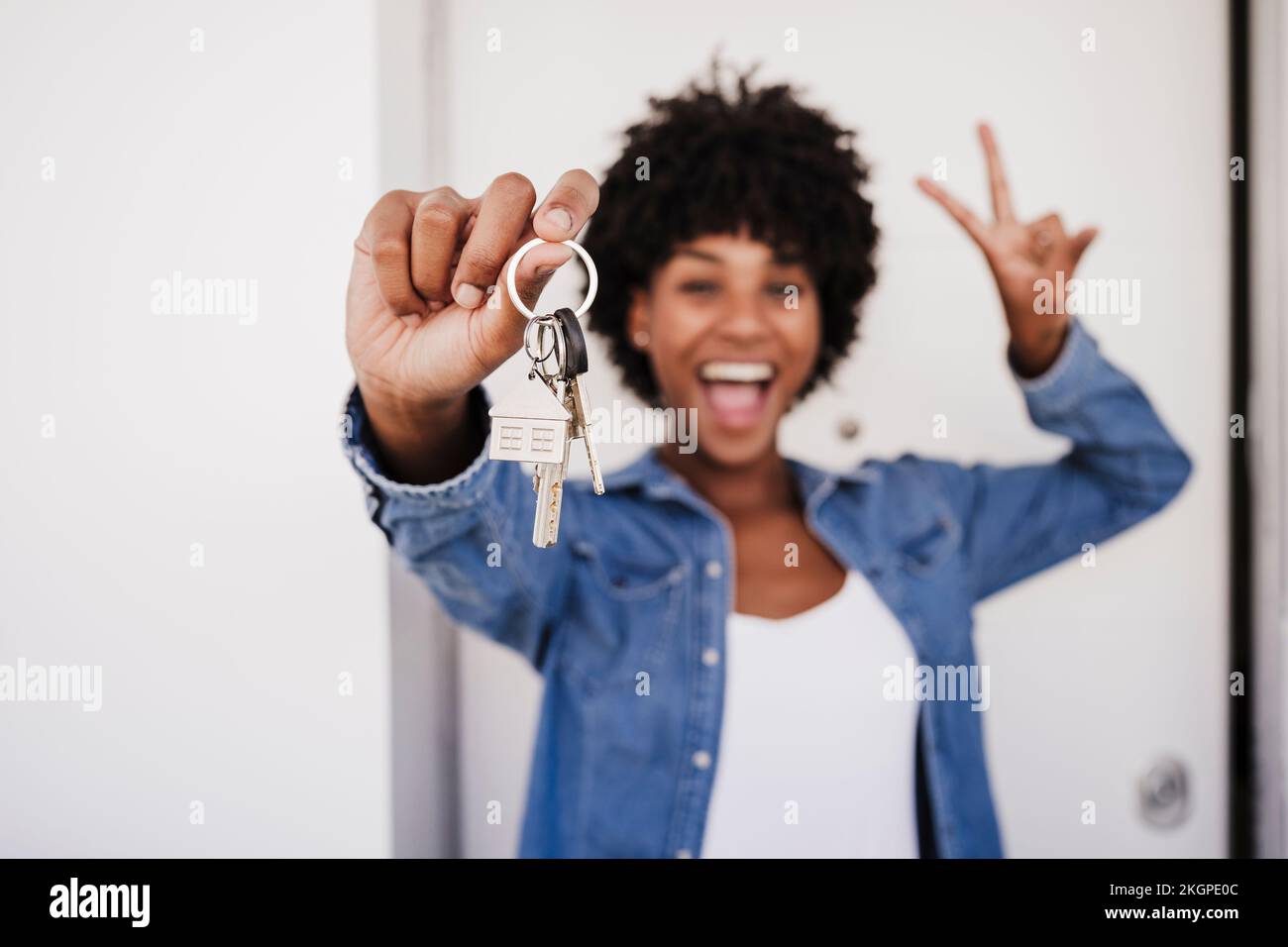 Donna allegra che mostra le chiavi della casa e segno di pace gesto di fronte alla porta Foto Stock