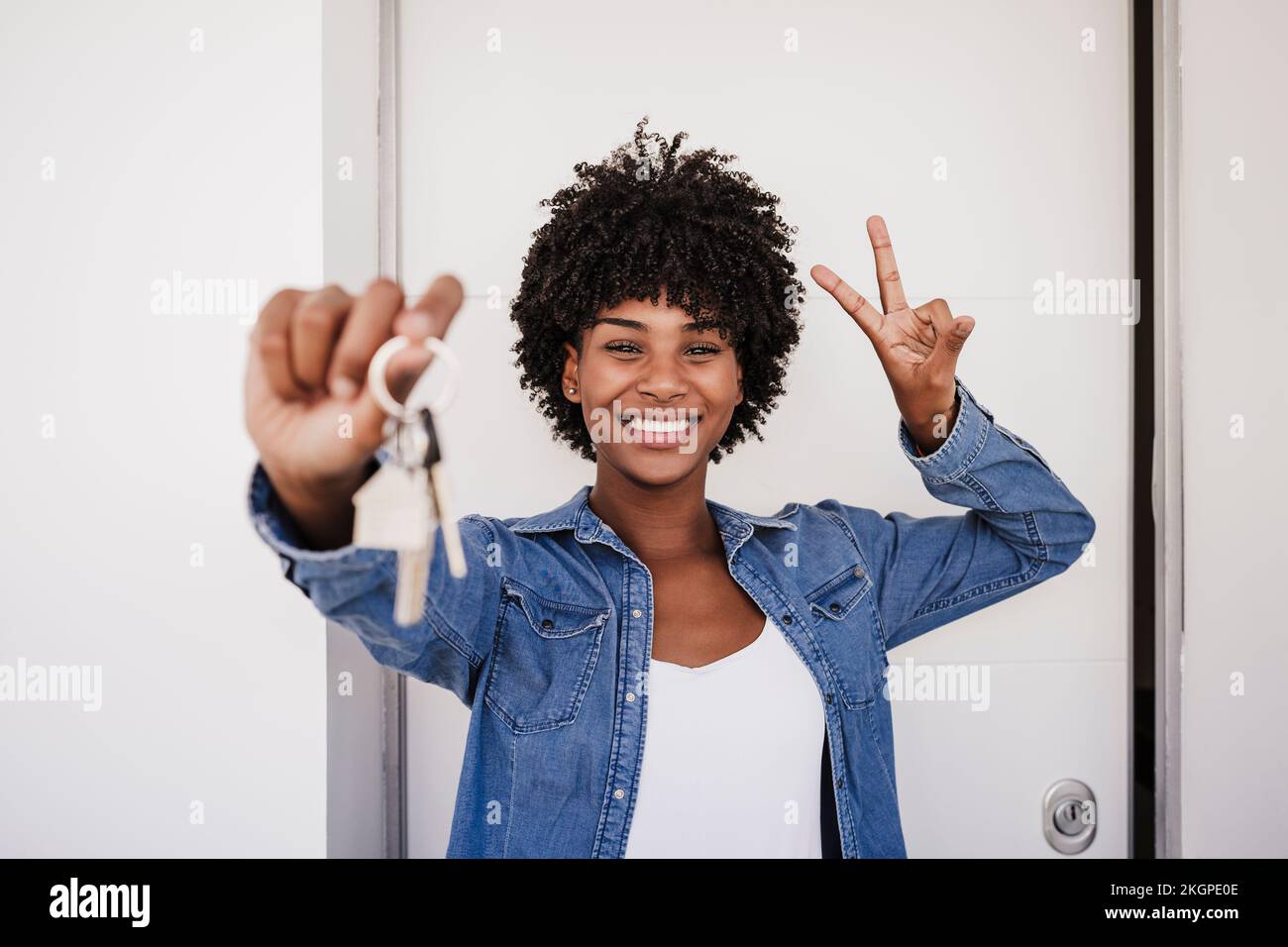 Donna felice che mostra le chiavi della casa e segno di pace gesto di fronte alla porta Foto Stock