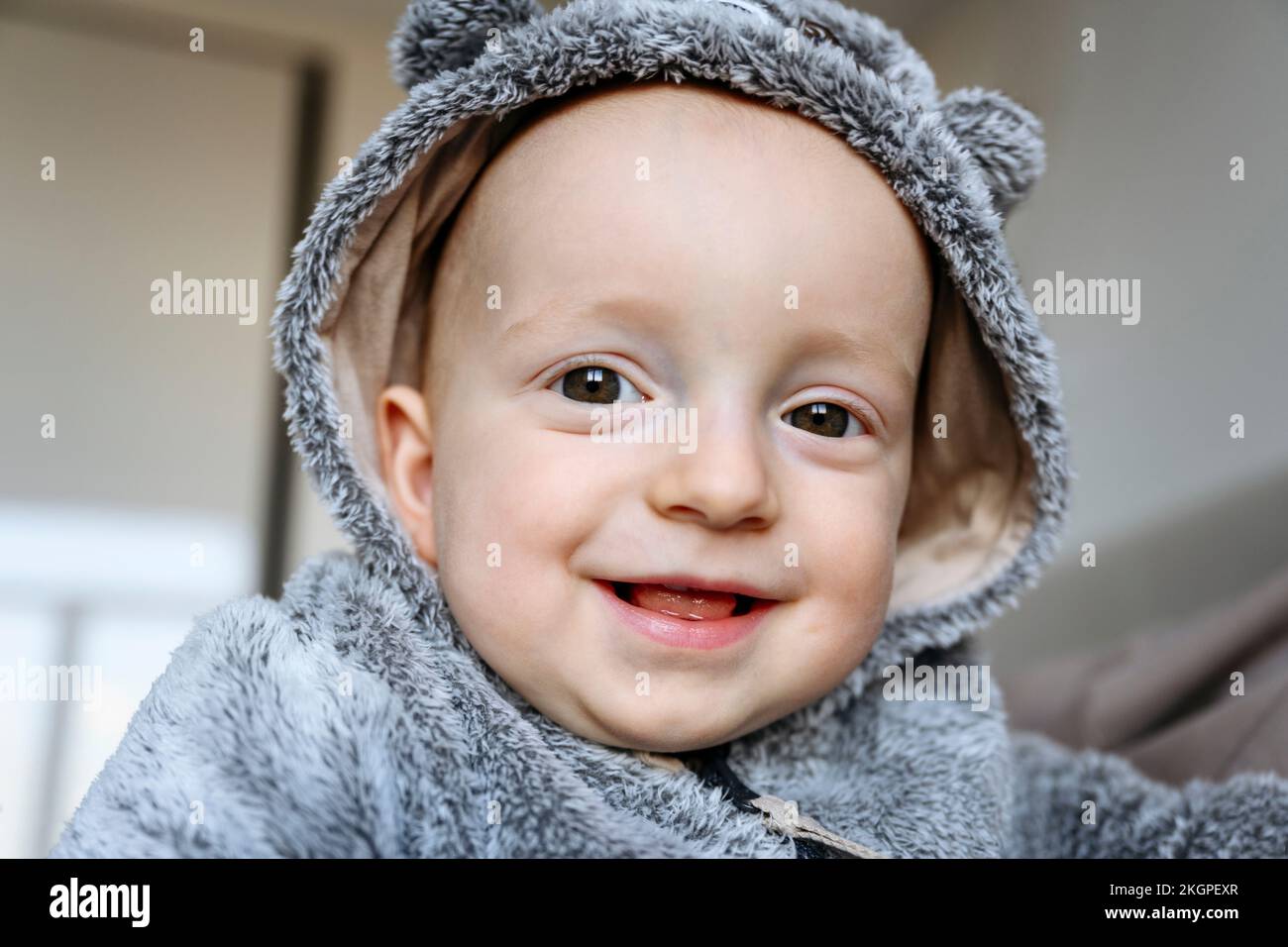 Ragazzo sorridente e carino che indossa il cappuccio grigio a casa Foto Stock