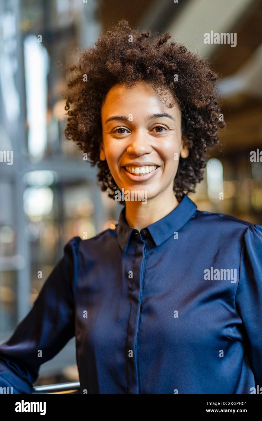 Donna d'affari felice con i capelli ricci che portano la camicia blu Foto Stock
