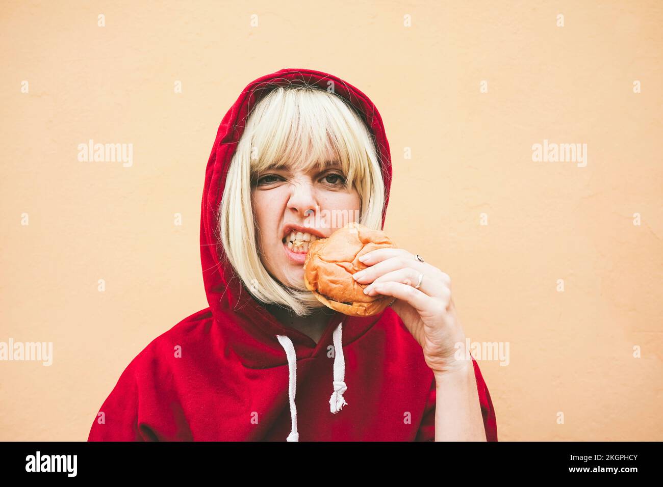 Donna che indossa una camicia con cappuccio rossa che mangia hamburger davanti alla parete della pesca Foto Stock