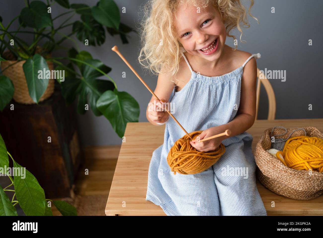 Ragazza felice che gioca con l'ago di maglia e la sfera di lana sul tavolo a casa Foto Stock