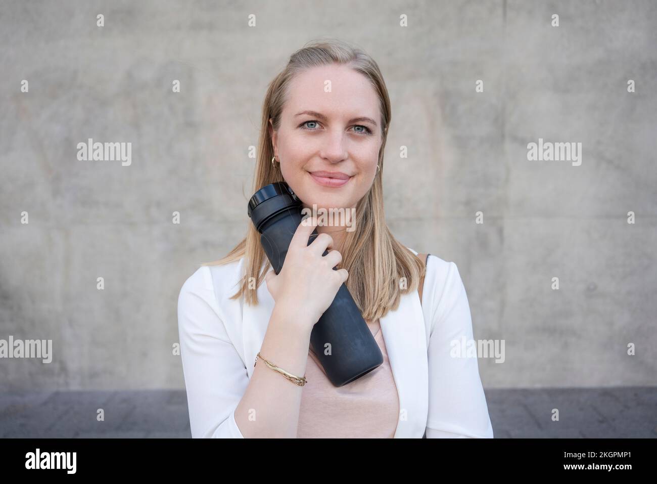 Donna sorridente con una bottiglia d'acqua riutilizzabile davanti alla parete Foto Stock