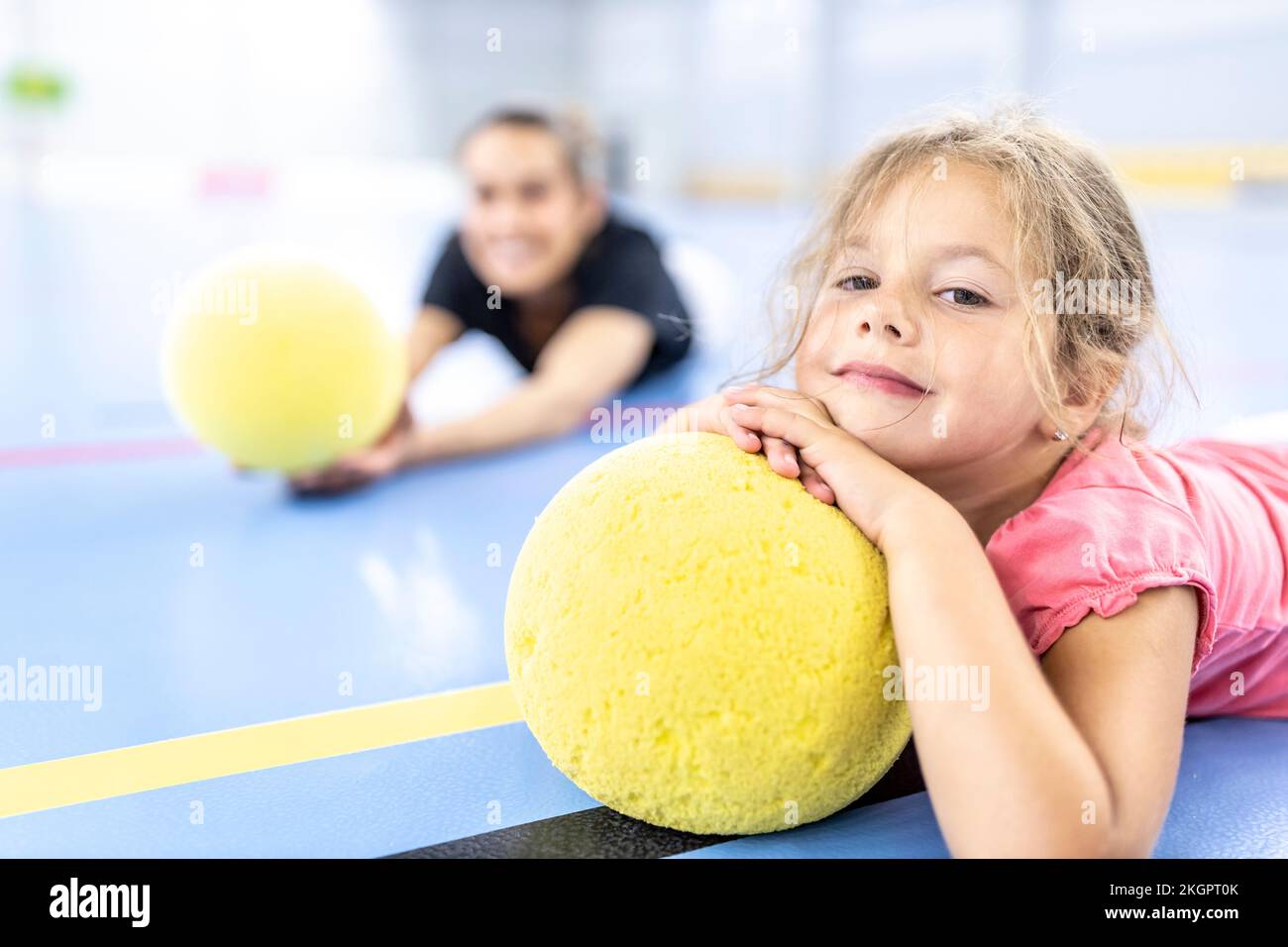 Ragazza che riposa sulla palla gialla sdraiata al campo sportivo della scuola Foto Stock