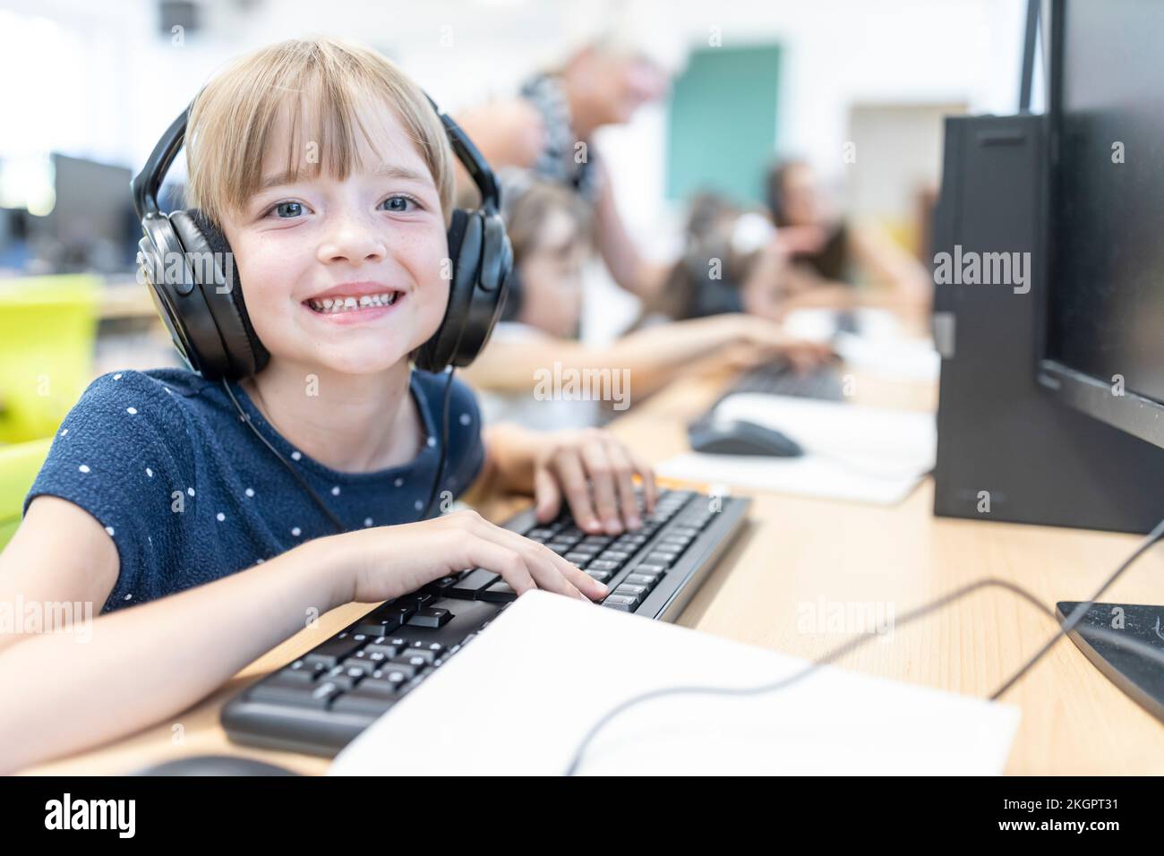 Felice studentessa elementare che indossa cuffie in classe computer a scuola Foto Stock