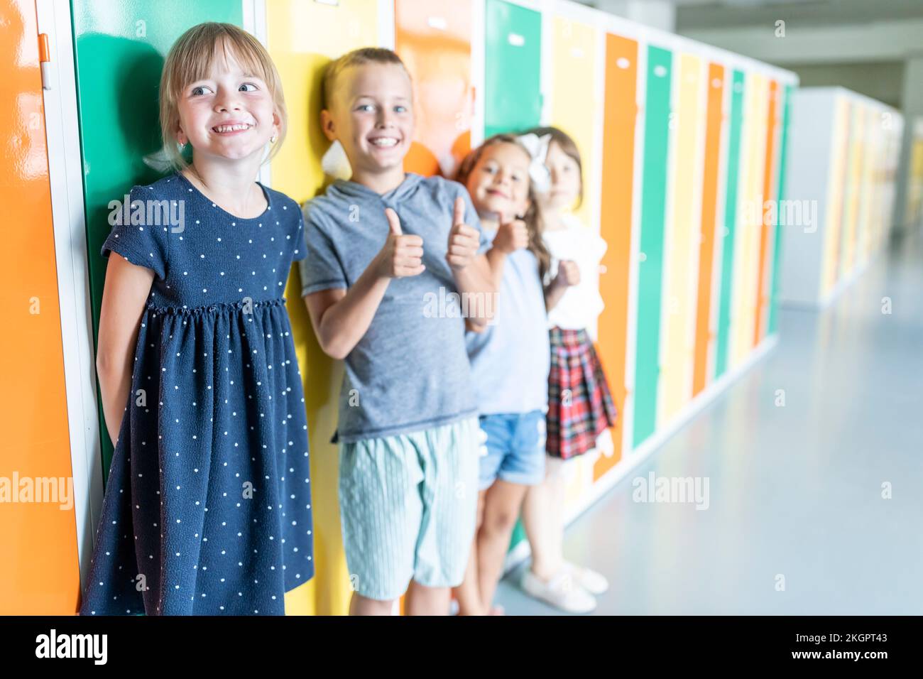 Studenti elementari felici in piedi vicino a colorati armadietti nel corridoio della scuola Foto Stock