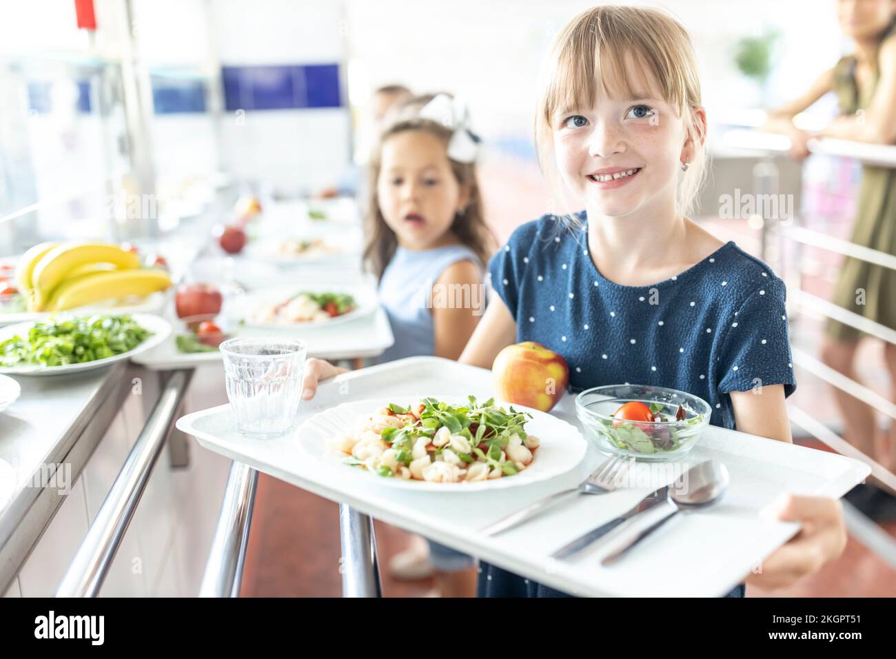 Ragazza sorridente che tiene il vassoio durante la pausa pranzo nella caffetteria della scuola Foto Stock