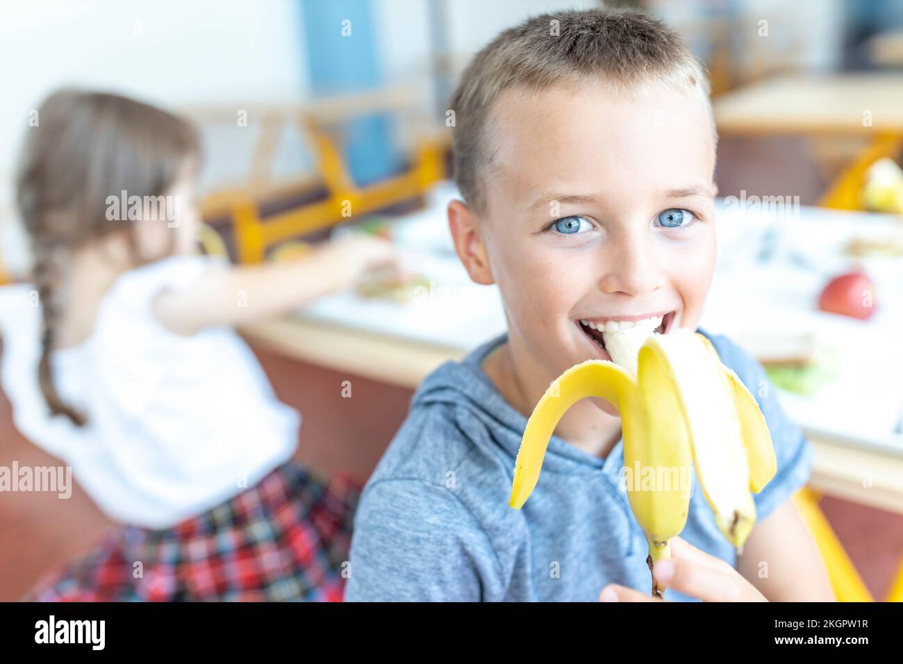 Ragazzo felice con occhi blu che mangia banana durante la pausa pranzo in caffetteria Foto Stock