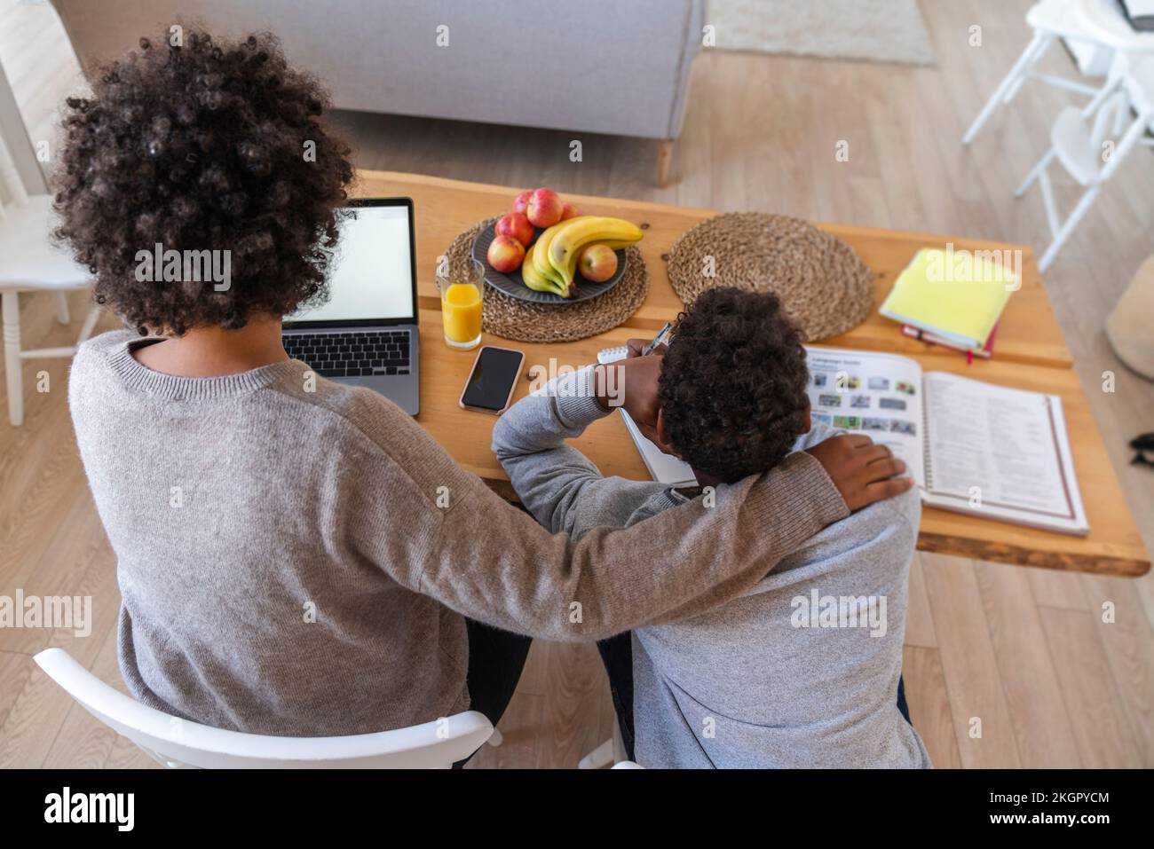 Madre seduta per figlio che fa lavoro di studio a casa Foto Stock