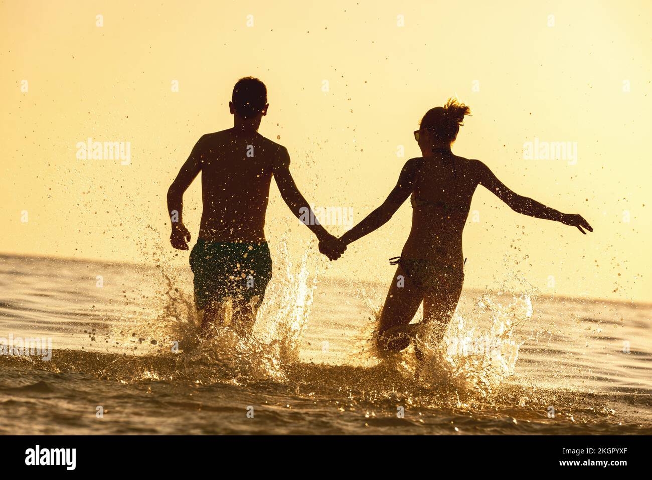 Felice giovane coppia corre al tramonto spiaggia di mare Foto Stock