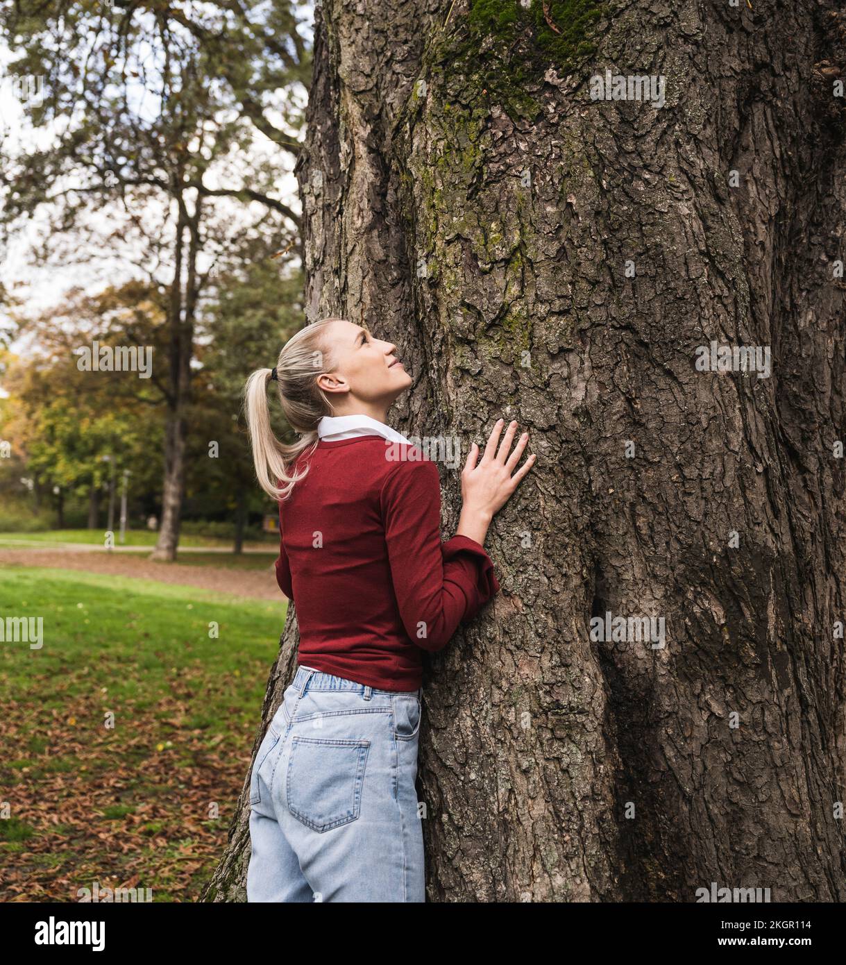 Giovane donna in piedi accanto all'albero nel parco Foto Stock