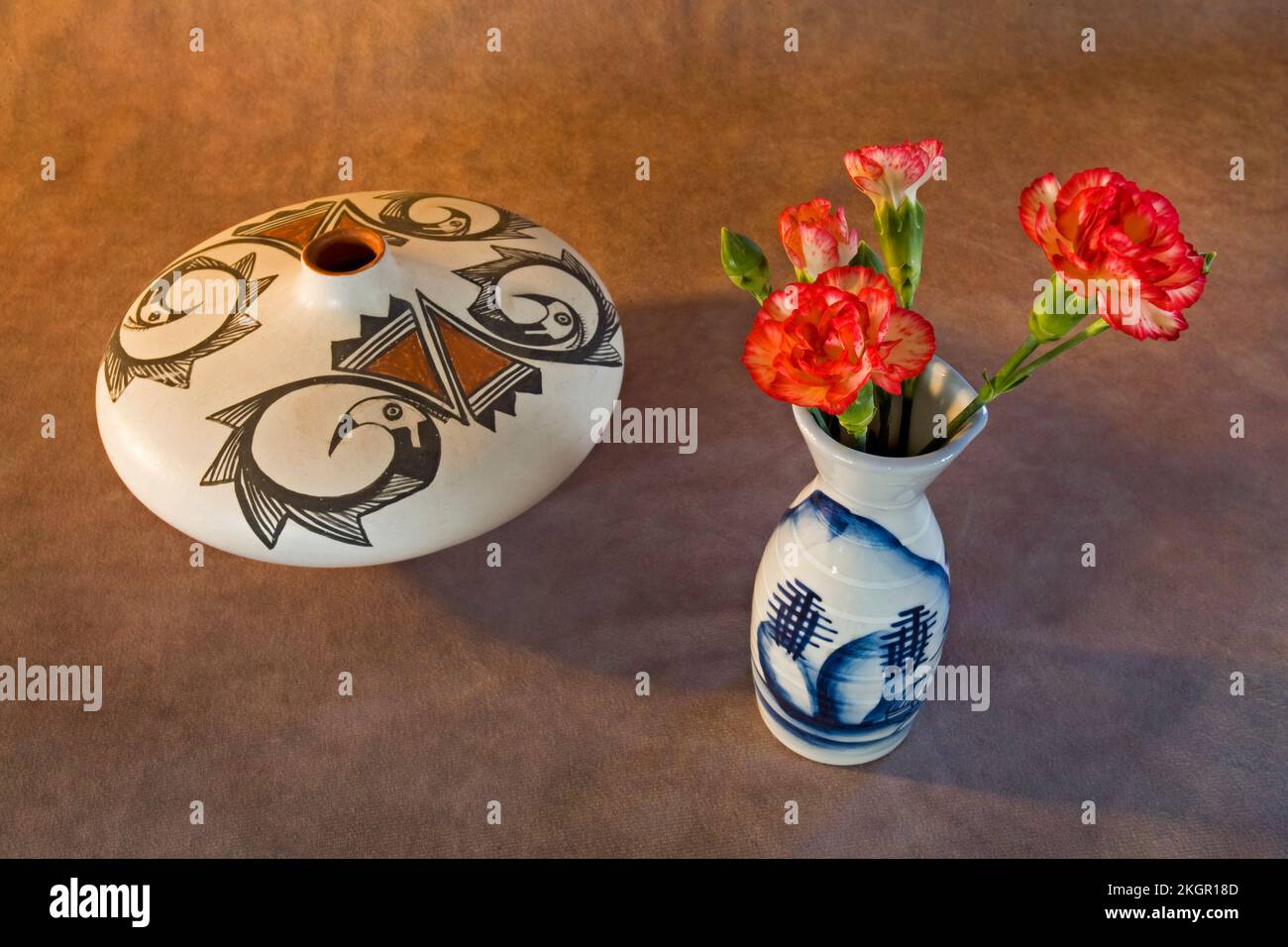 Un vaso di garofani e un vaso di stoccaggio di semi Pueblo indiano di Acoma su uno sfondo scuro. Foto Stock