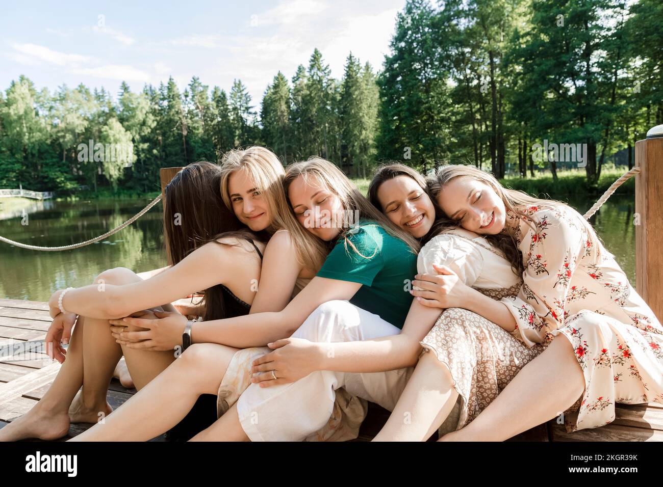 Giovani amici sorridenti che si abbracciano da dietro sul molo Foto Stock