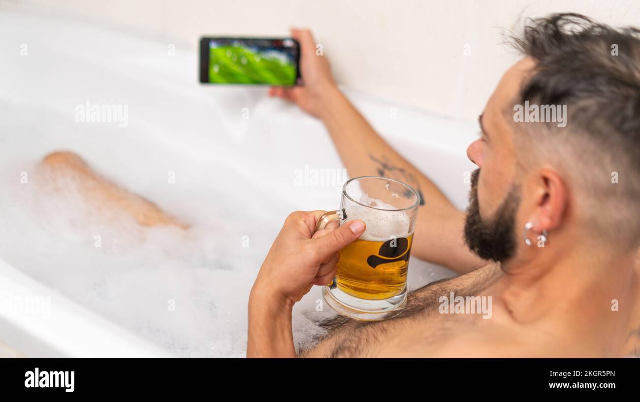 Uomo bearded che guarda il calcio con la birra in bagno Foto Stock