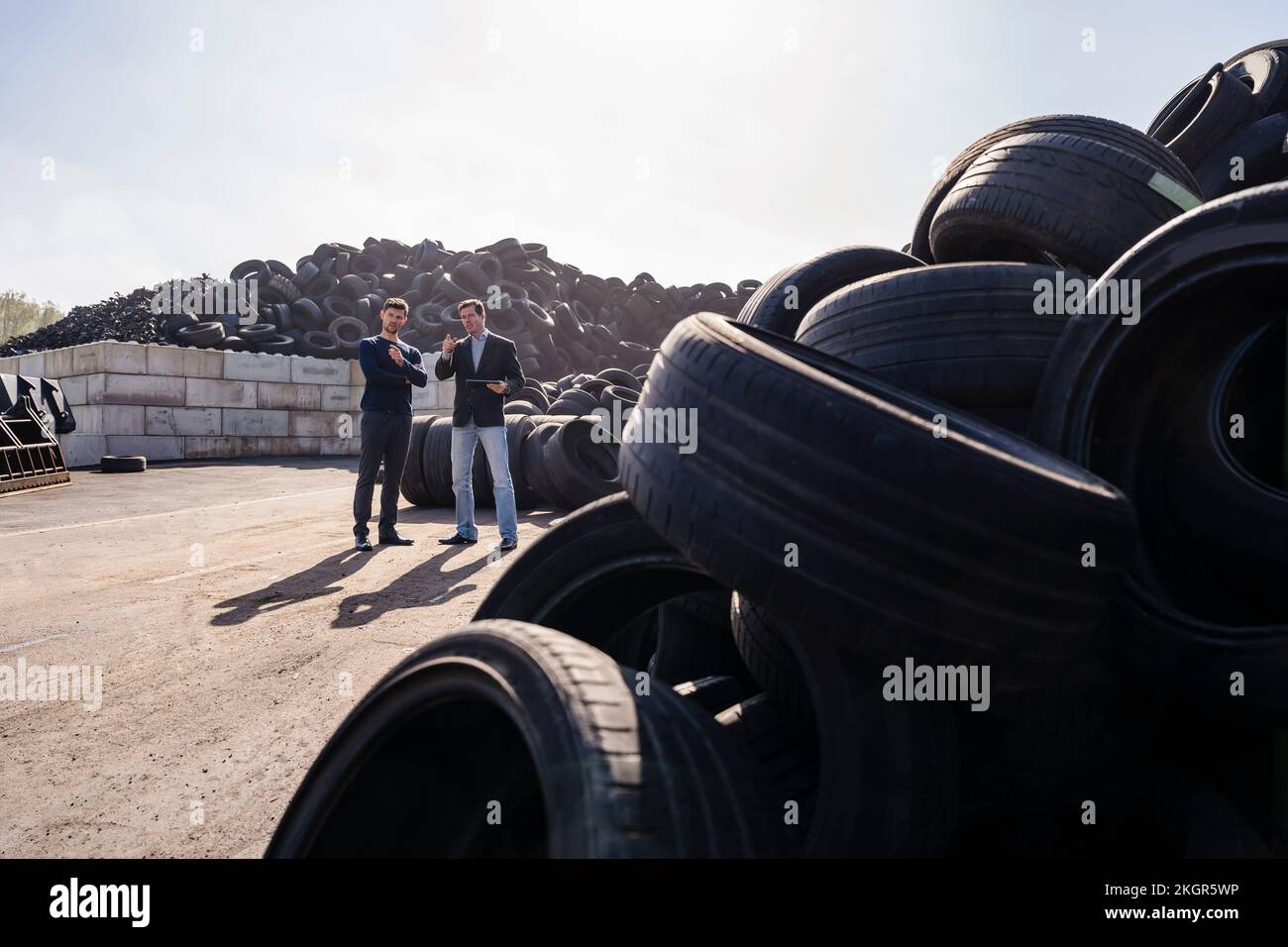 Uomini d'affari che discutono sopra il mucchio delle gomme di gomma all'impianto di riciclaggio Foto Stock