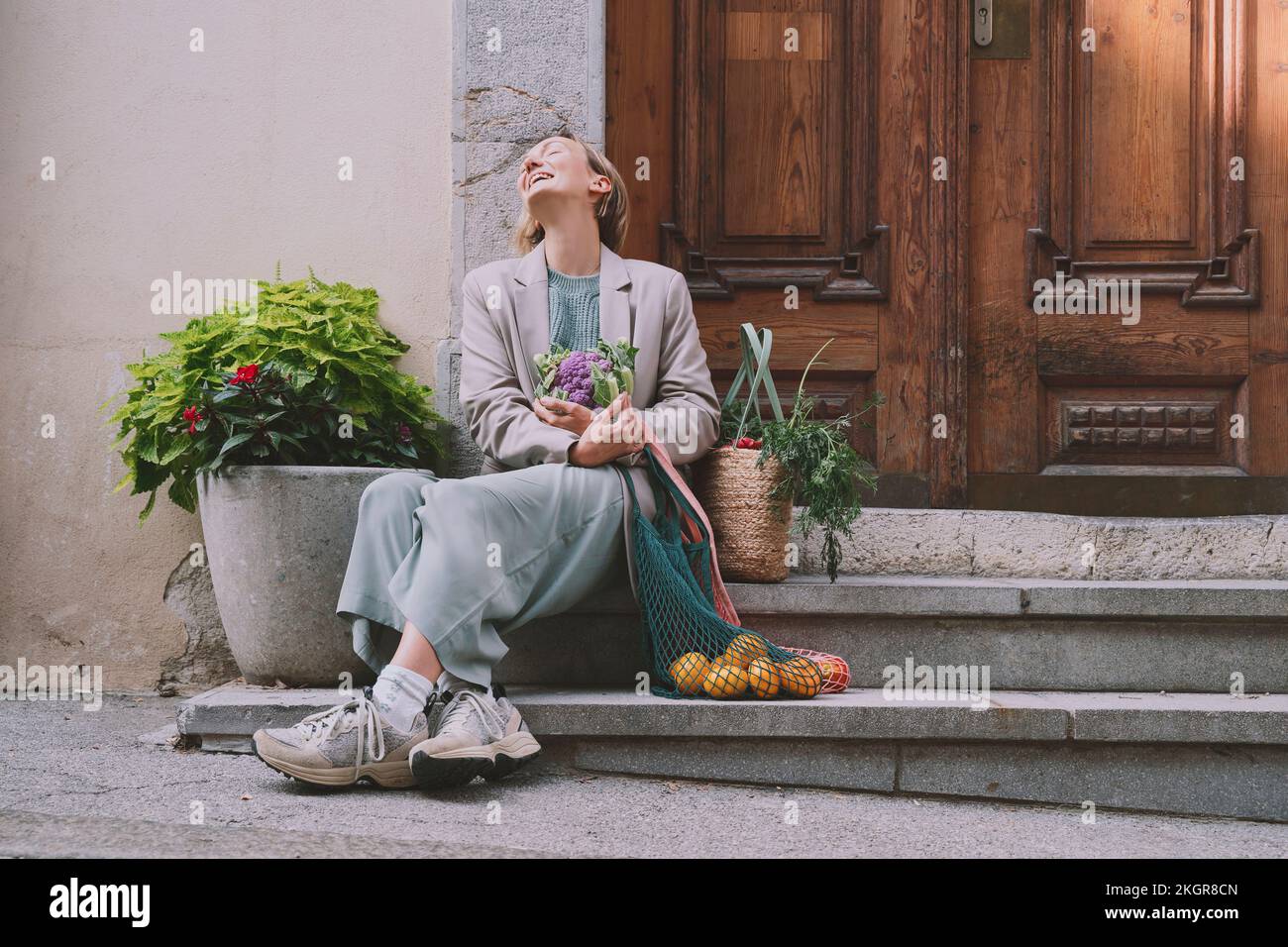 Donna felice che tiene cavolfiore seduto con verdure e borse di frutta sulla scala Foto Stock