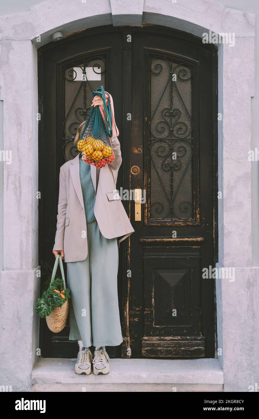 Donna che copre il viso con una borsa a rete piena di arance davanti alla porta Foto Stock